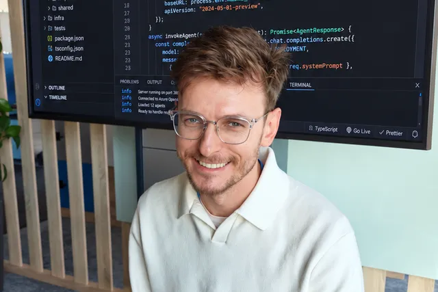Rafał Bogusz at a desk in front of a screen showing TypeScript code